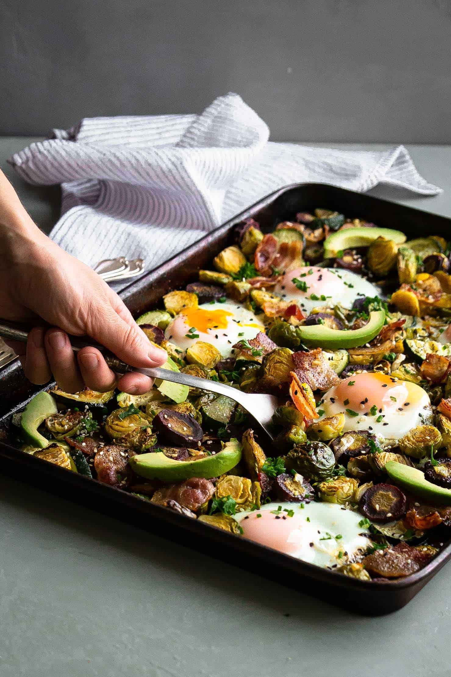 I've got something to really kick up your weekend brunch or weekday breakfast plans: the best paleo one pan breakfast bake. It is full of delicious and healthy fats, protein and nutrient dense veggies. It's low carb, Whole30 compliant and perfect for a quick and easy breakfast meal! sheet pan with eggs, avocado and vegetables bring scooped out with a fork