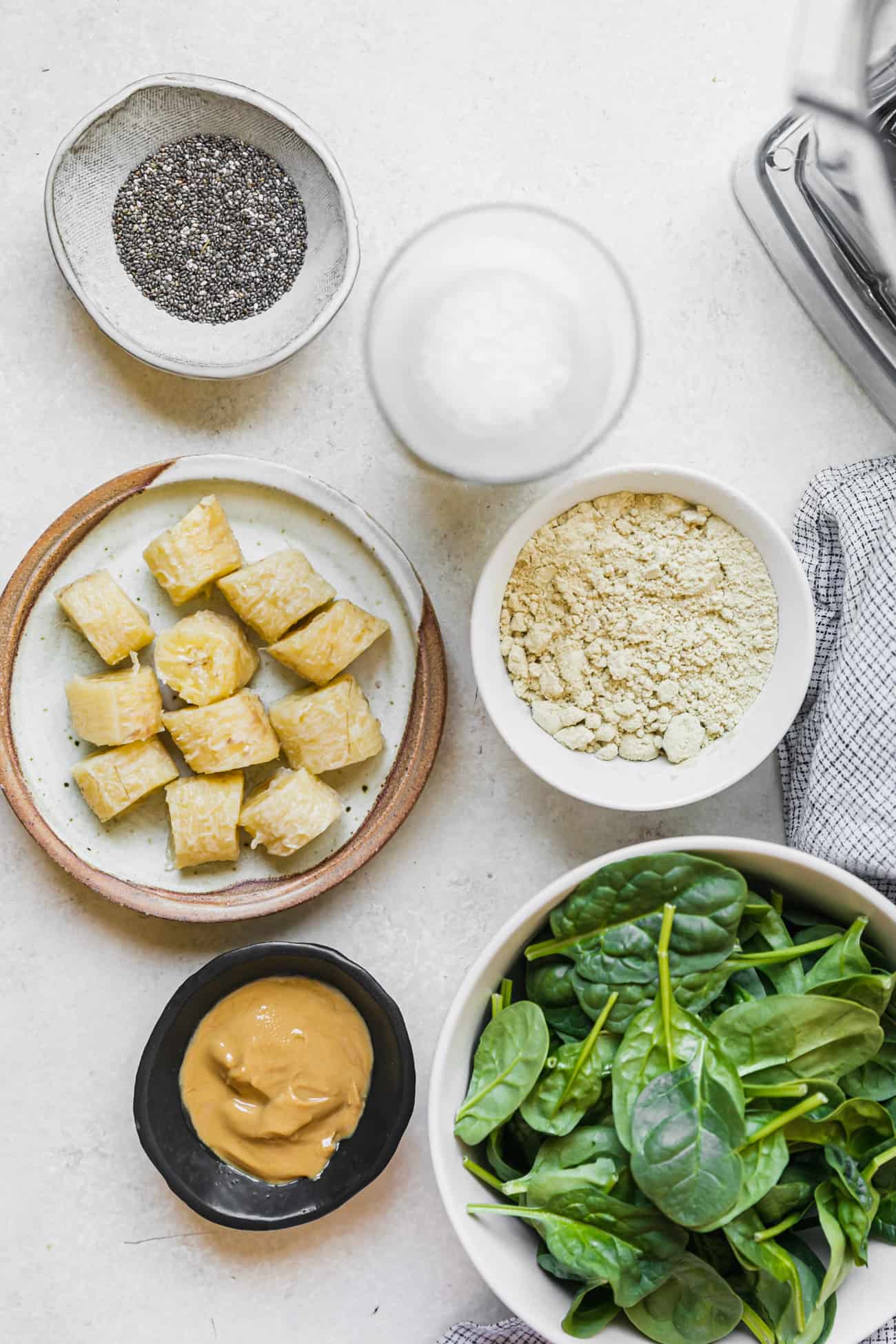 ingredients prepped to make a spinach and banana smoothie: spinach, nut butter, milk, banana, collagen, and chia seeds.
