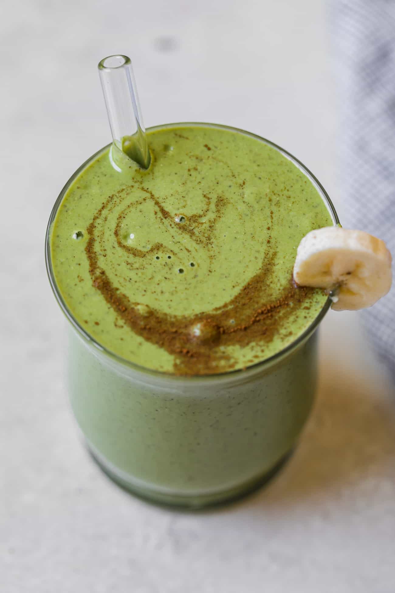 banana spinach smoothie in a cup with a glass straw