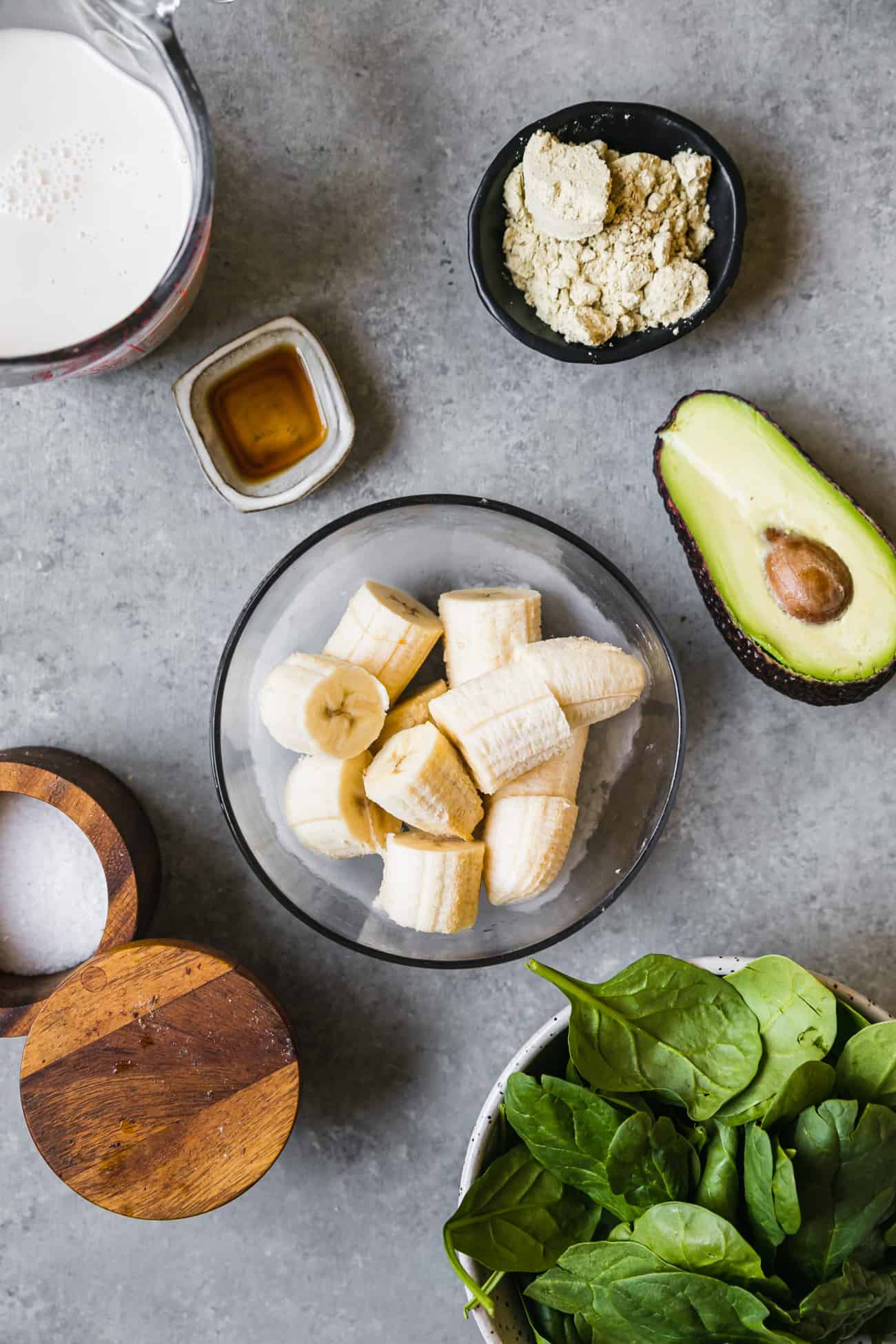 ingredients prepped to make avocado smoothie: frozen banana, avocado, salt, spinach, protein, vanilla, milk