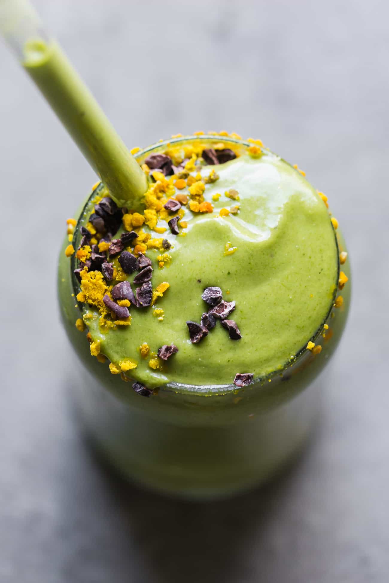 creamy green smoothie in a glass cup with a glass straw and bee pollen